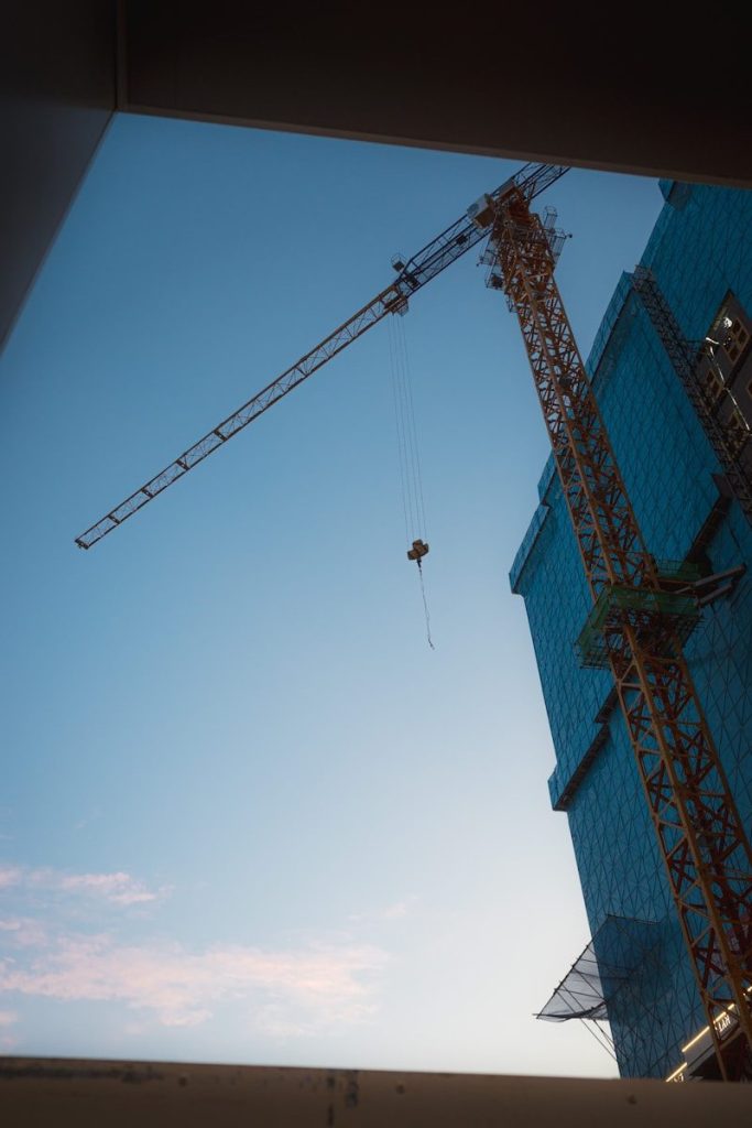 Construction crane and blue-netted building against clear sky.